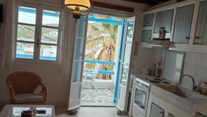 A kitchen with a stone floor, white cabinets, and a view of a balcony with a palm tree. - Ornos Beachside 2 Bd Stylish House (Mykonos)