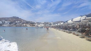 A beach with clear water, sun loungers, and a row of beachside shops. - Ornos Beachside 2 Bd Stylish House (Mykonos)