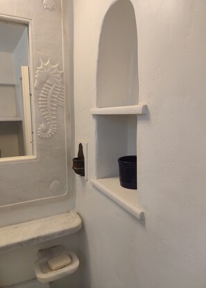 Une salle de bain avec une porte blanche, un miroir, un porte-savon et une étagère sur laquelle se trouve un récipient bleu.