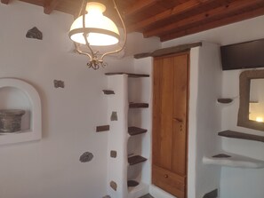 Une pièce avec une porte en bois, des éléments décoratifs en pierre sur les murs, une étagère et un miroir fixé au mur.