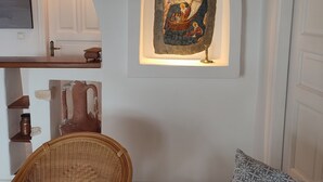A room with a white wall, a wooden ceiling, a wicker chair, a patterned cushion, and a stone artwork. - Ornos Beachside 2 Bd Stylish House (Mykonos)