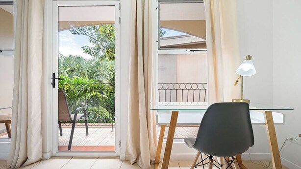 A room with a glass door leading to an outdoor area with a view of greenery. Inside, there is a desk with a chair and a lamp. - Villa Verde 1#8 (Tamarindo)