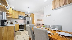 A modern kitchen with wooden cabinets, a built-in microwave, and a dining area with grey chairs and a wooden table set for four. - Villa Verde 1#8 (Tamarindo)