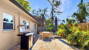Une terrasse avec un barbecue, une table et des chaises d’extérieur, entourée d’une clôture en bois et de verdure.