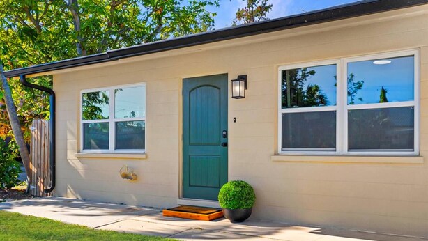 Une maison de plain-pied avec une porte verte, deux fenêtres, un petit porche orné d’un pot de fleurs et une boîte aux lettres bien visible.