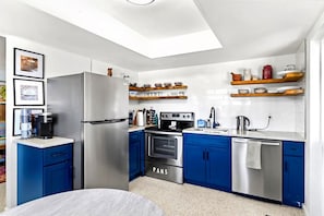 A modern kitchen with a stainless steel refrigerator, oven, and dishwasher, blue cabinets, and a skylight.