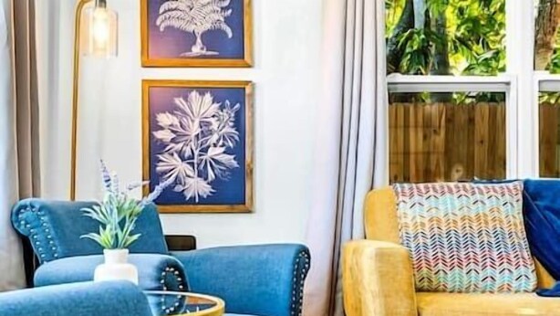 A living room with a blue sofa, a yellow sofa, and a small round table with a plant. There are two framed artworks on the wall. - Charming Villa 14 mins away from Siesta Key Beach (Sarasota)