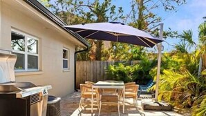 A patio with a table and chairs, a grill, and a covered area with an umbrella. - Charming Villa 14 mins away from Siesta Key Beach (Sarasota)