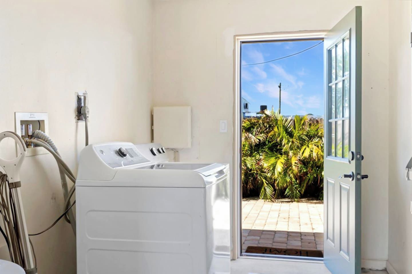 A laundry room with a washing machine, a dryer, and a door leading to a patio with plants.