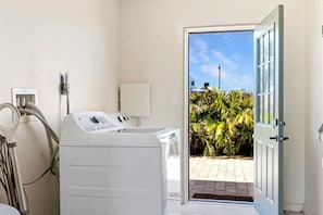 A laundry room with a washing machine, a dryer, and a door leading to a patio with plants.