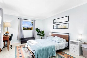 A bedroom with a bed, bedside tables, a desk, a chair, a window with curtains, and a view of the outdoors.