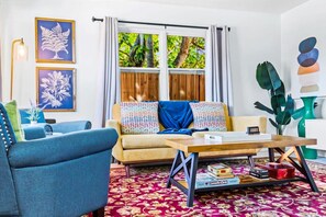 A living room with a sofa, armchair, coffee table, and a view of greenery outside.