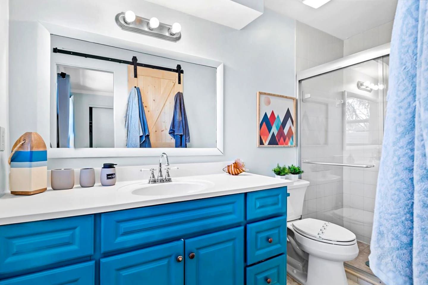 Une salle de bain moderne avec un lavabo blanc, des meubles bleus, une douche en verre et un porte-serviettes avec des serviettes.