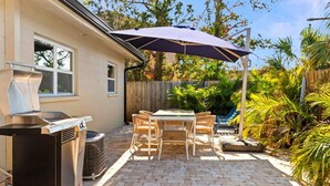 Une terrasse avec un barbecue, une table d’extérieur et un parasol.