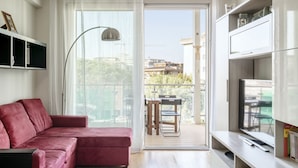 A modern living room with a red sofa, a TV on a stand, and a balcony with outdoor furniture.