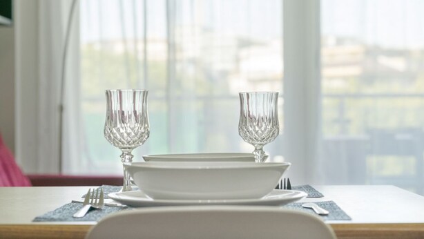 A dining table set with white plates, two clear glassware, and a fork and knife on a placemat.