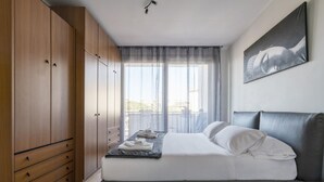 A bedroom with a bed, a wardrobe, a window with curtains, and a wall-mounted artwork.