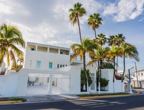 A modern building with a white facade, multiple windows, and a gated entrance.
