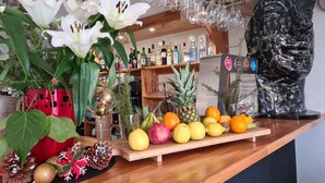 A bar area with a wooden counter, a variety of fruits, a pineapple, and a decorative statue. - LE BON DUC (Les Billaux)
