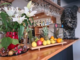 Una zona de bar con una barra de madera, diversas frutas, una piña y una estatua decorativa.