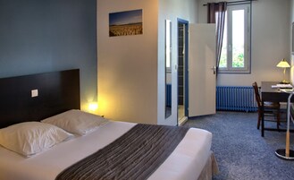 Habitación de hotel con cama, escritorio, silla, radiador y ventana con cortinas.