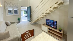 A modern living room with a staircase, a sofa, a TV on a wooden stand, and a potted plant. - Pistachio Suite - Town Centre (Corfu)