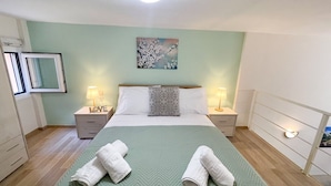 A bedroom with a bed, two bedside tables, a nightstand, a painting, and a window. - Pistachio Suite - Town Centre (Corfu)