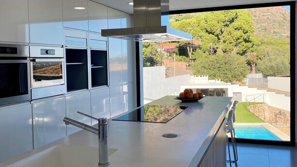 A modern kitchen with a large island, built-in ovens, and a view of a swimming pool and greenery.