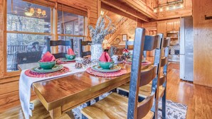 Une salle à manger en bois avec une grande table dressée pour quatre personnes, entourée de chaises.