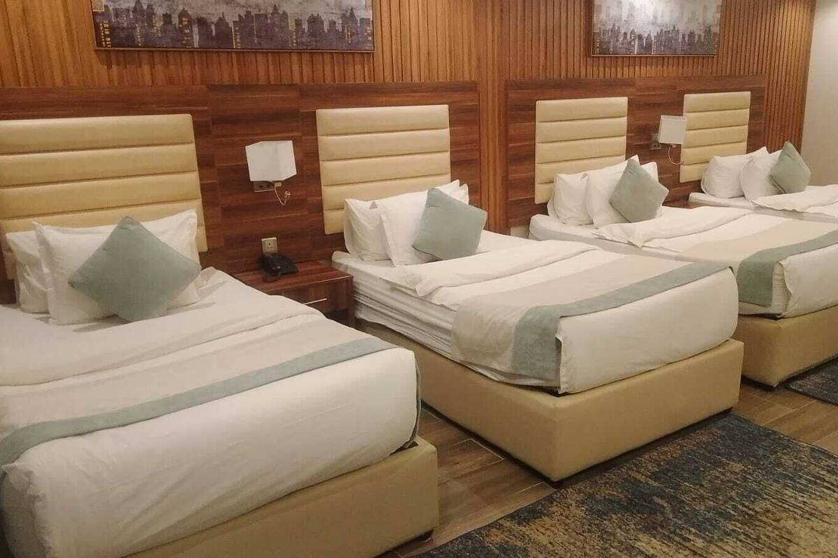 A hotel room with four beds, each with a headboard and bedside tables.