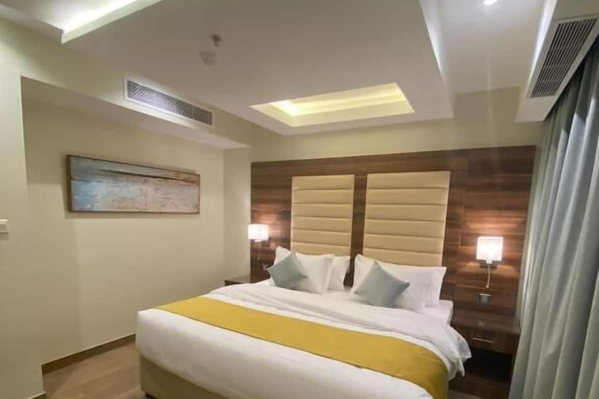 A hotel room with a large bed, a bedside table, a wall-mounted artwork, and a ceiling light.