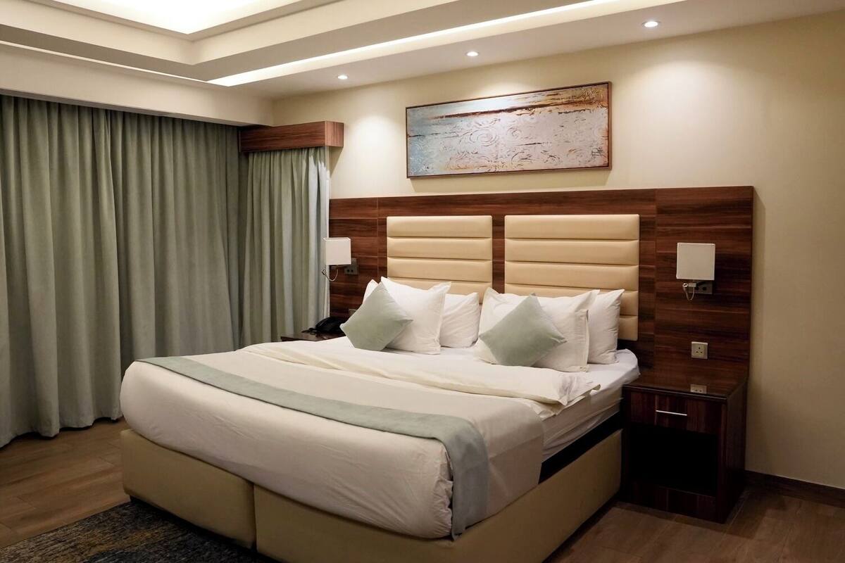 A hotel room with a large bed, wooden headboard, and a painting on the wall.