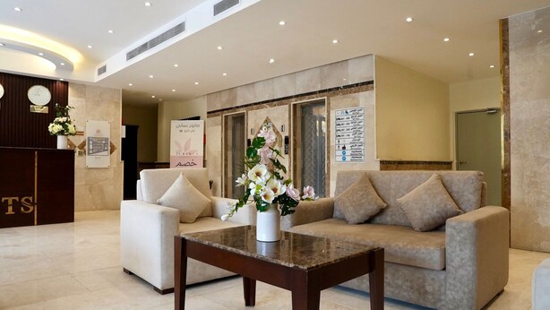 Un lobby moderno con una recepción, dos sofás, una mesa de centro y un jarrón decorativo con flores.