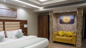A modern bedroom with a large bed, a wooden wardrobe, a yellow sofa, and a stone accent wall with artwork. - Moments Hotel  (Jeddah)