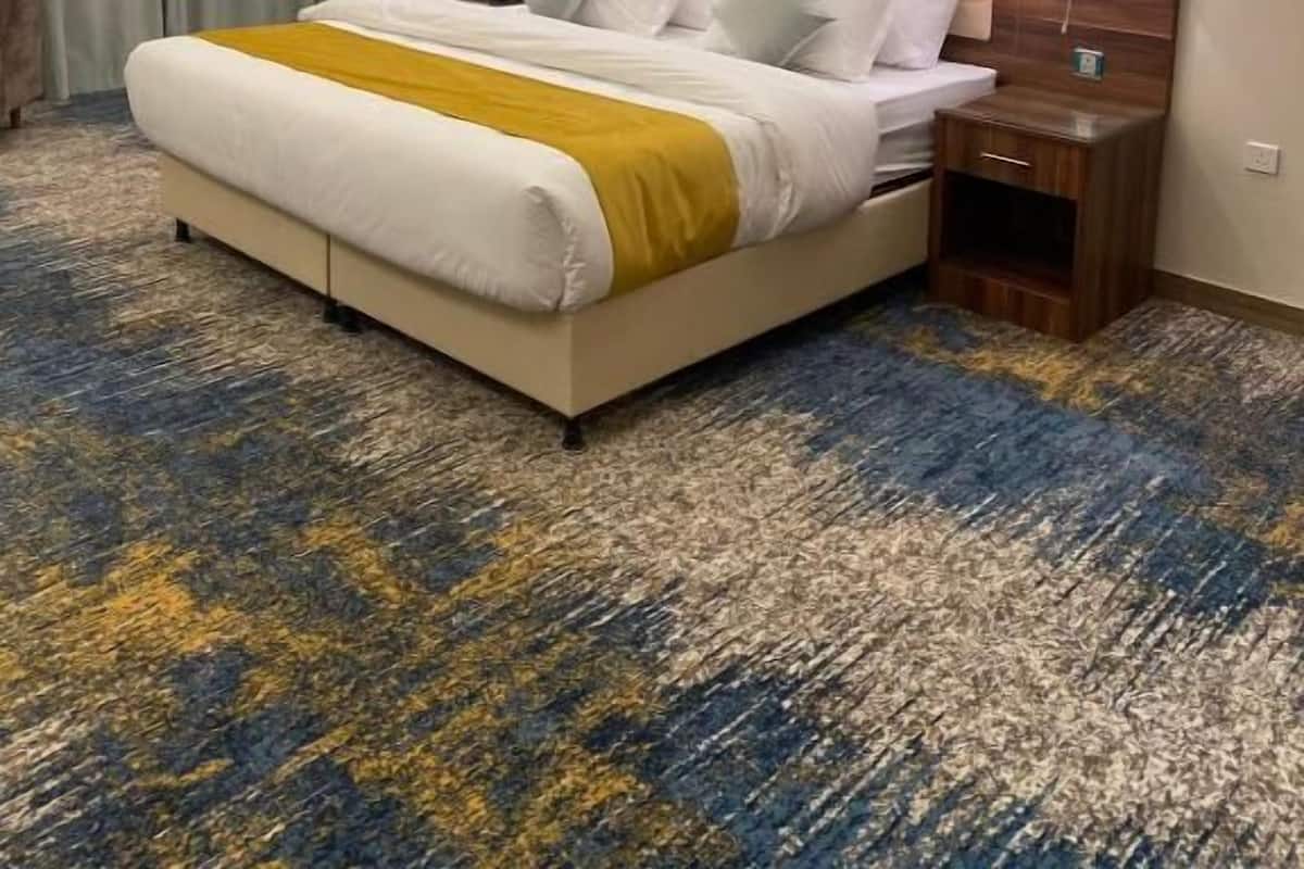 A hotel room with a large bed, a headboard, two bedside tables, a painting on the wall, and a patterned carpet.