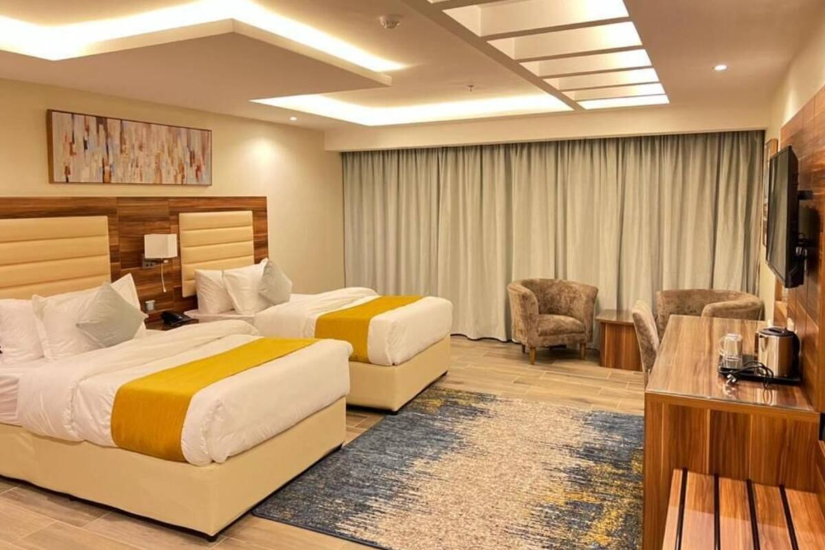 A hotel room with two beds, a desk, a chair, a TV, and a large window with curtains.