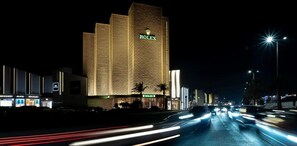 Un hotel de gran altura con una fachada distintiva, señalización iluminada y una calle concurrida al frente.