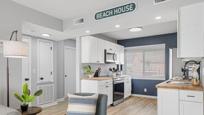 A modern kitchen with white cabinets, a stove, and a microwave. There is a sign above the kitchen that reads "BEACH HOUSE". - A Little Shore Thing- 1 Bed Oceanfront Condo (Carolina Beach)