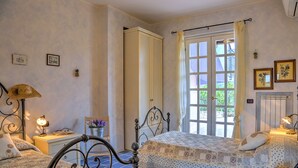 Une chambre à coucher avec un lit, une table de chevet, une lampe, une chaise et une fenêtre avec des rideaux.
