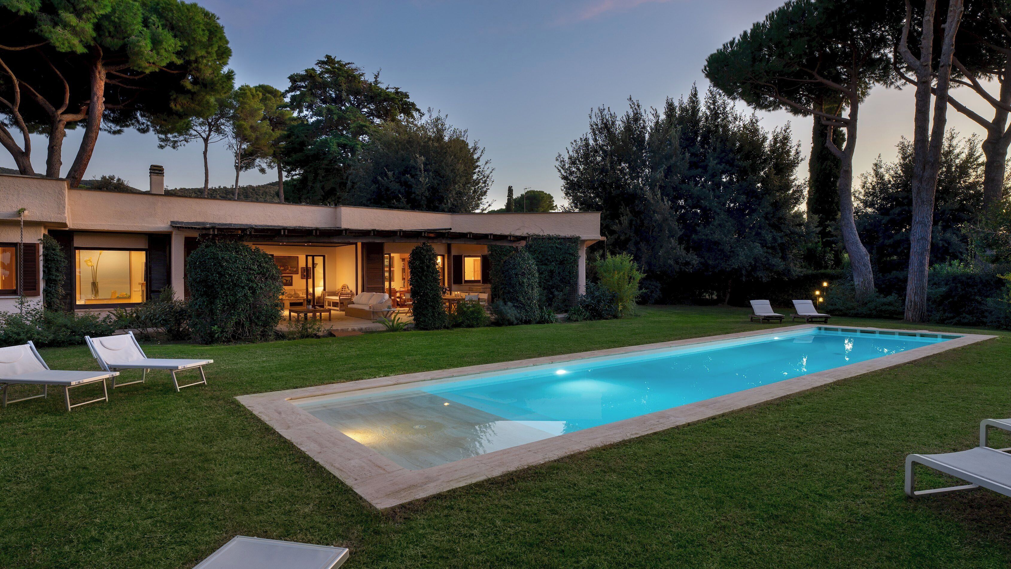 Una casa moderna amb piscina, un patio amb mobiliari exterior i un jardí ben cuidat.