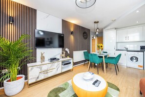 A modern living room with a TV, sofa, dining table, and kitchen area. - Hide Out Two Bed Apartment at ExCeL (London)