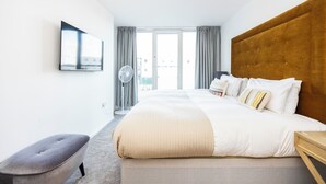 Ett modernt hotellrum med en stor säng, en platt-TV som är monterad på väggen, ett nattduksbord i trä och en grå klädd bänk.