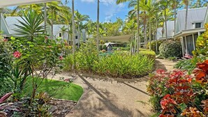 Un jardín con palmeras, un sendero y un edificio de techos inclinados.