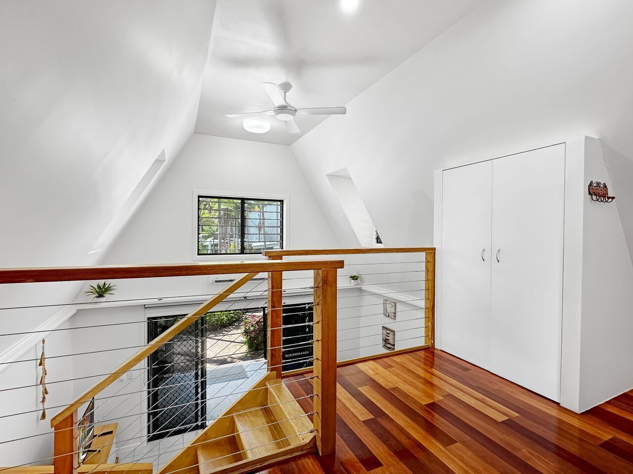 A modern interior with a wooden staircase, a ceiling fan, and a white wardrobe.