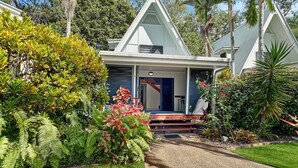 Una casa moderna con un llamativo techo triangular, rodeada de exuberante vegetación y un jardín cuidado.