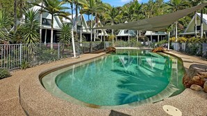 Piscina rodeada de palmeras y una valla, con cielo despejado.