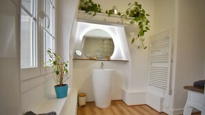 A bathroom with a white sink, a mirror, a potted plant, and a window.