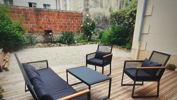 An outdoor patio with a wooden deck, a black sofa, two black chairs, and a small table.