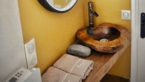 Une salle de bain avec un meuble-lavabo en bois, un miroir rond et un lavabo en pierre.