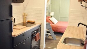 Une cuisine de taille réduite avec un réfrigérateur noir, un plan de travail en bois et un petit évier.